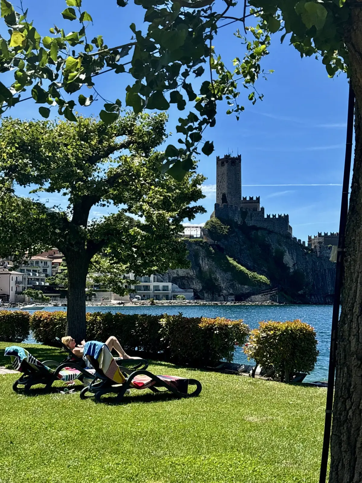 Lettini all'ombra sul prato del lido, con il Castello Scaligero sullo sfondo